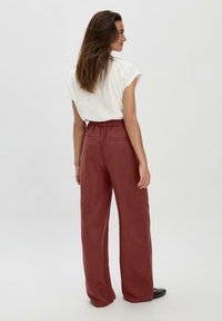 Losse, hooggeplaatste, roestkleurige broeken van zacht materiaal, met een gerimpelde tailleband en twee achterzakken.