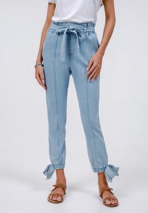 Pantaloni jogger in denim blu chiaro con vita alta, cintura da annodare e polsini elastici, caratterizzati da aperture laterali legate con fiocchetti coordinati.