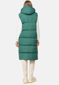Gilet verde lungo con cappuccio, design trapuntato e maniche bianche. Indossato sopra pantaloni fitted chiari e calzature chunky.