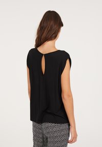 Blusa nera a maniche corte con scollatura rotonda e un piccolo dettaglio a chiave sul retro. Tessuto morbido con una vestibilità ampia.