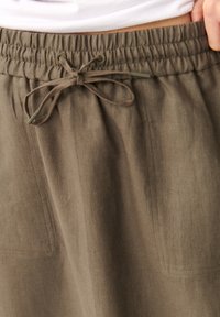 Hnedé ľanové nohavice s elastickým pásom a nastaviteľným šnúrkovým uzáverom. Obsahujú bočné vrecká a majú ľahký textil.