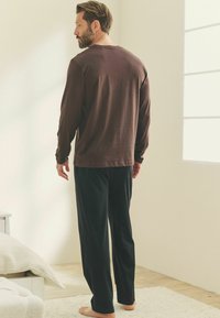 Langærmet brun skjorte parret med sorte bukser. Begge er lavet af blødt stof, har en afslappet pasform og et minimalistisk design.