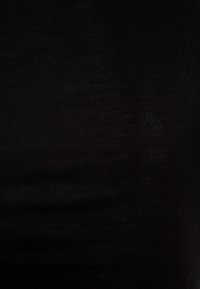 Tissu tricoté noir affichant une texture lisse. Le matériau semble légèrement transparent avec de subtiles variations de lumière. Aucun motif ni accent présent.