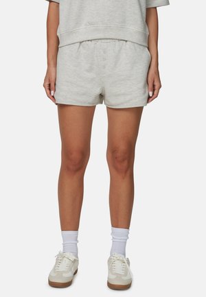 Lichtgrijze katoenen shorts met een elastische tailleband, knoopdetails aan de voorkant en een losse pasvorm. Gecombineerd met witte sneakers en sokken.