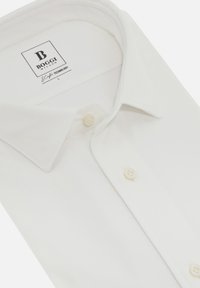 Camicia bianca con colletto classico. Realizzata in tessuto testurizzato, presenta due bottoni color crema e un'etichetta con il marchio "Boggi Milano".