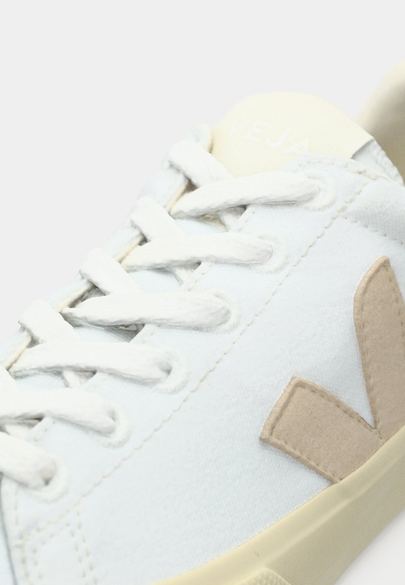 Sneaker bianca con tomaia testurizzata, dettagli in suede beige e lacci di tessuto. Il nome del marchio è stampato in colore chiaro sulla linguetta.