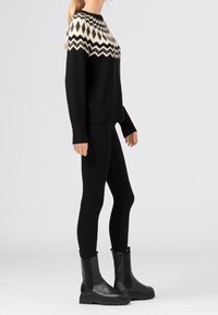 Svart stickad tröja med ett vitt zickzackmönster vid halsringningen, kombinerad med svarta leggings och svarta robusta ankelboots.