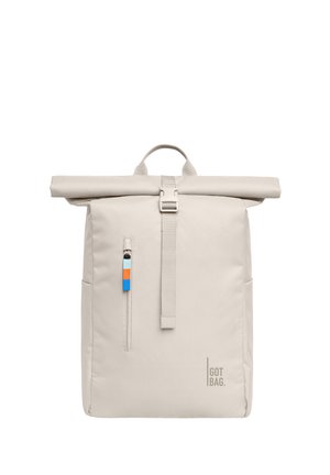 Sac à dos beige à rabat roulé avec poche zippée verticale sur le devant, languette de tirette tricolore, poignée supérieure et logo "GOT BAG" dans le coin inférieur droit.
