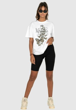 Hvid oversized t-shirt med et sommerfugleprint, parret med sorte biker shorts og beige sneakers med høj top.