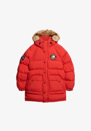 Rote Daunenjacke mit einer Kapuze mit Fellbesatz, ausgestattet mit einem runden Logo auf der Brust, Druckknöpfen und zwei Fronttaschen.