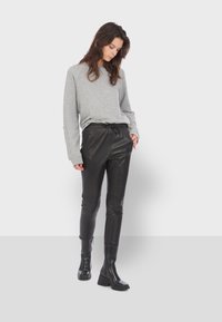 Šedá mikina s dlouhým rukávem v kombinaci s černými koženými kalhotami s elastickým pasem. Model nosí černé kotníkové boty na vysokém podpatku; hladké textury po celém outfitu.