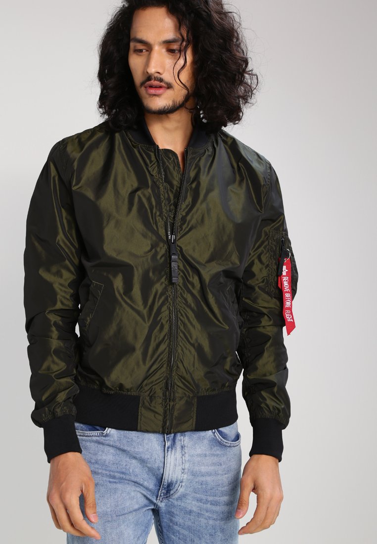 Olive green bomber jacket with a zip front, ribbed cuffs, and hem. Features patch pocket on sleeve with red tag detail. Shiny, smooth fabric.