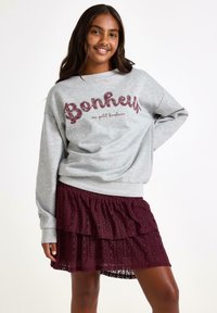 Grå sweatshirt med "Bonheur" tekst i bourgognirød glimmer, parret med en bourgognirød lagdelt blonde nederdel. Behagelig pasform, afslappet design.