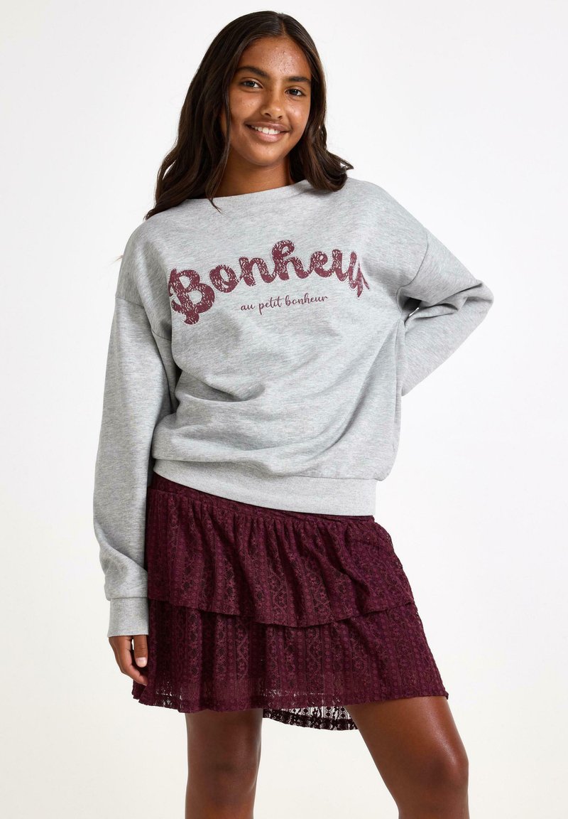 Grå sweatshirt med "Bonheur" tekst i bourgognirød glimmer, parret med en bourgognirød lagdelt blonde nederdel. Behagelig pasform, afslappet design.