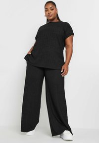 Mustat kaksiosaiset vaatteet, joissa on teksturoitu lyhythihainen paita pyöreällä kaula-aukolle ja leveälahkeiset housut, molemmat rentoa istuvuutta.