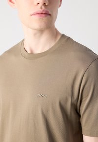 Vihreä khaki puuvillapaita, jossa on pyöreä pääntie, lyhyet hihat ja pieni "BOSS"-logo samaa väriä vasemmalla puolella.