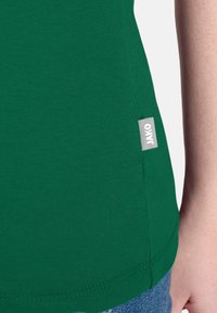 T-shirt in cotone verde con tessuto testurizzato; presenta un'etichetta JAKO sul lato della cucitura e un orlo curvo. Design semplice e aderente.