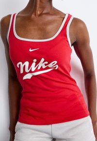 Röd ribbad linne med en kontrasterande grå kant och en vit "Nike"-logotyp över framsidan. Tyget verkar mjukt och sittande.