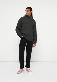 Mørkegrå strikket turtleneck sweater, sorte bukser og lyserøde high-top sneakers. Stoffet har et struktureret mønster, der skaber et hyggeligt udseende.