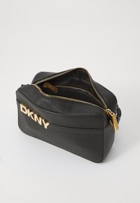 Melnas ādas kosmētikas somiņa ar zelta DKNY logotipu, divām rāvējslēdzēju nodalījumiem un teksturētu virsmu. Rāvējslēdzēji ar zelta dekoratīvām detaļām.