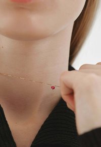 Collar de cadena de oro con una pequeña piedra preciosa rosa en forma de corazón, usado cerca del cuello, sobre una prenda negra texturizada.