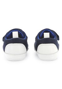 Mornarsko platnene tenisice s bijelim gumiranim potplatima; sadrže bijelu oznaku straga i trake s čičak zatvaranjem za jednostavno oblačenje.