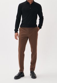 Svart långärmad pikétröja med knappar, kombinerad med smala bruna byxor och svarta loafers. Slät tyg och skräddarsydd design.