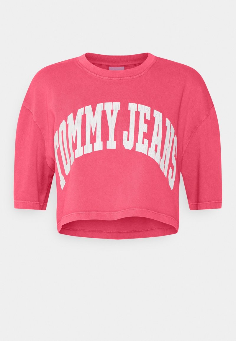 T-shirt cropped à manches courtes en coton rose vif, avec le texte blanc "TOMMY JEANS" sur le devant dans un design arrondi.