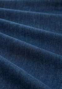 Tela de mezclilla azul oscuro con una textura suave, que presenta ligeras variaciones en la tonalidad, mostrada en capas dobladas.