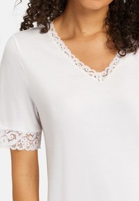 Top corto bianco a maniche corte con scollatura a V, rifinito con delicate pizzi e dettagli in pizzo sulle maniche, realizzato in un tessuto morbido e leggero.
