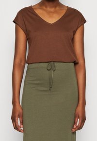 Camiseta marrón de cuello en v con mangas cortas, combinada con una falda larga de color verde oliva con cordón ajustable, hecha de una tela suave y elástica.