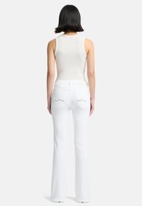 Weiße, ausgestellte Jeans mit detaillierter Naht auf den Gesäßtaschen, kombiniert mit einem taillierten weißen Tanktop, das eine glatte, gerippte Textur zeigt.