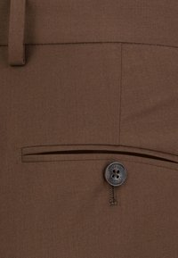 Brązowe spodnie materiałowe z płaską kieszenią zapinaną na guzik. Gładka faktura z dopasowanymi szwami i pętlą na pasek w pasie.