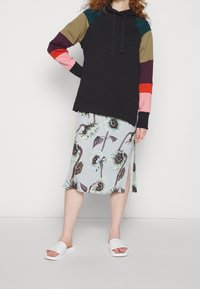 Felpa nera con cappuccio e maniche multicolori; gonna azzurra chiara a fantasia floreale con girasoli; sandali bianchi con fascia.