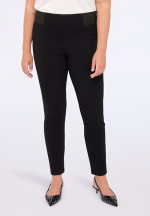 Schwarze, maßgeschneiderte Hose mit einem hohen, strukturierten Bund. Slim-Fit, der sich bis zum Knöchel verjüngt, kombiniert mit spitzen schwarzen Absätzen mit Nietenakzenten.