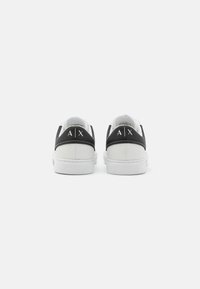 Sorte og hvite joggesko med en strukturert overdel, som har en glatt hvit såle og preget logo på hælen. Rundt tådesign.
