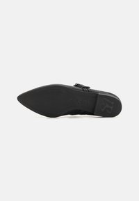 Sole di scarpa nera a punta con superficie in gomma testurizzata. Presenta un logo goffrato discreto e un design elegante, che enfatizza il minimalismo.