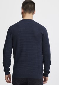 Tumesinine tekstuuriga sviiter ümaral kaelusel ja pikade varrukatega. Omab soonikvarrukaid ja äärt, seljal on kudumise muster.