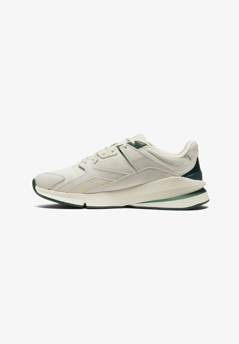 Baskets de sport beige avec des dessus en maille et en cuir, accents texturés, détail au talon vert, et semelle en caoutchouc blanc avec une bande contrastante.