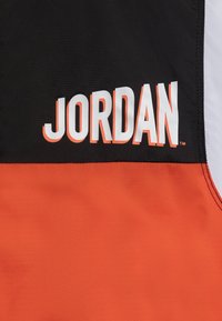Black and orange fabric with "JORDAN" printed prominently in bold white letters. Features a smooth texture and contrasting color blocks.