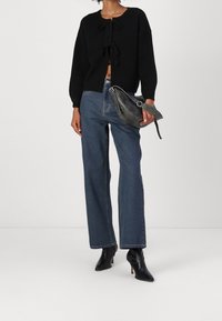 Cardigan negro de punto con cierre de lazo, combinado con jeans de pierna recta de talle alto azules y botas de tobillo negras. Bolso gris con correa.