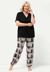 Schwarzes kurzärmeliges Top mit V-Ausschnitt, kombiniert mit gemusterten Schlafanzughosen in Pastellfarben mit geometrischen und floralen Designs.