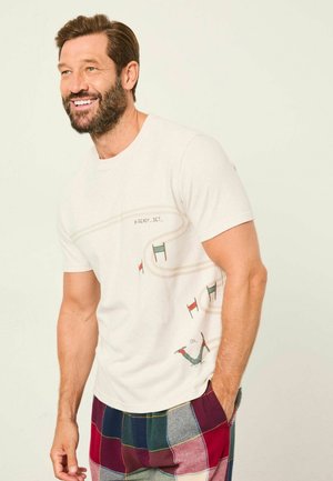 White cotton t-shirt featuring a design with colorful skiing gates and a playful figure, paired with plaid flannel pants in various colors.