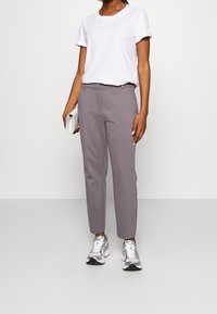 Grå avsmalnande sweatpants med en mjuk yta, kombinerat med en vit t-shirt med rund halsringning och en silverfärgad kuvertväska. Bärs med grå och gröna sneakers.