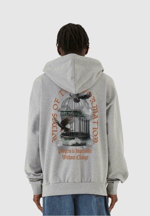 Grå hætte sweatshirt med et grafisk design af et fuglebur, fugle og tekst på ryggen. Blødt materiale med en afslappet pasform og ribbet manchett.