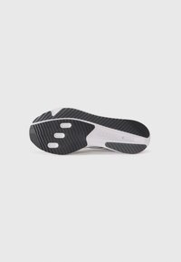 Black and white athletic shoe sole featuring textured rubber with ridges, identifying logo, and three circular accents for traction.