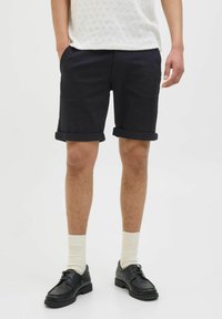 Navy cotton shorts with rolled cuffs, accented by a white textured knit shirt and black shoes, complemented by light-colored socks.