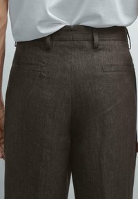 Dark brown linen trousers with a textured finish, featuring two back pockets and a tailored fit. Pairs well with casual or formal attire.