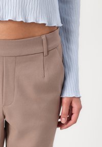 Haut à manches longues texturé bleu clair avec un ourlet volanté associé à un pantalon beige ajusté à finition lisse et poches latérales.