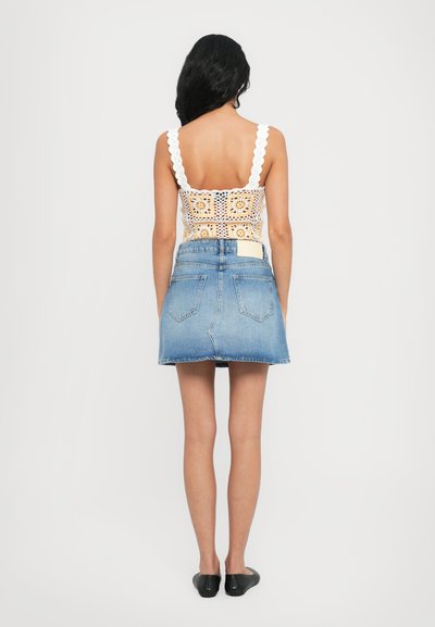 Jupe en denim au design ajusté, de couleur bleu clair, avec un ourlet brut. Le haut présente un motif en crochet blanc avec des bretelles à volants et une doublure.